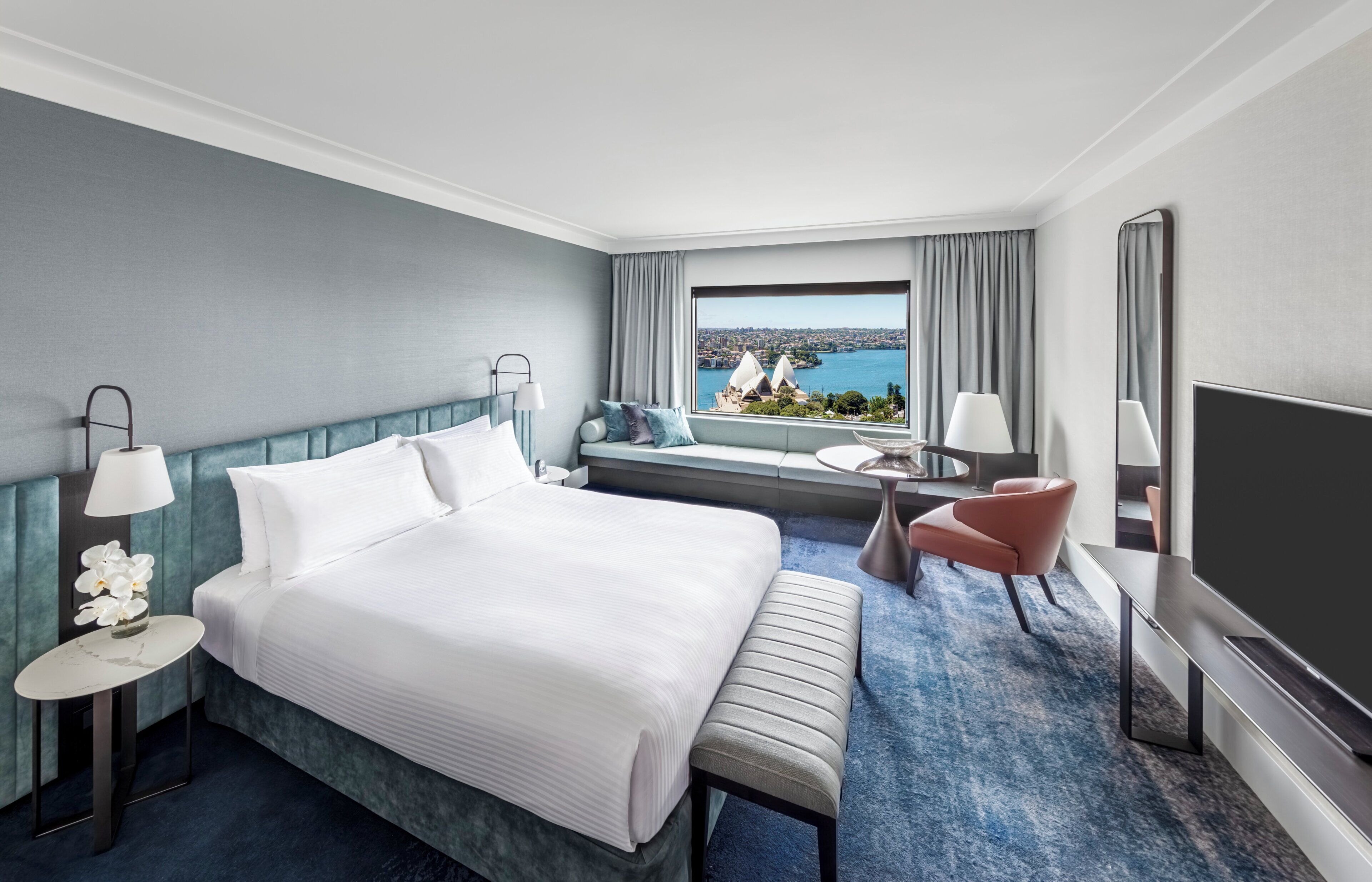 Habitación de hotel con una cama grande, zona de estar con vista a un paisaje urbano y al agua, y un televisor de pantalla plana.
