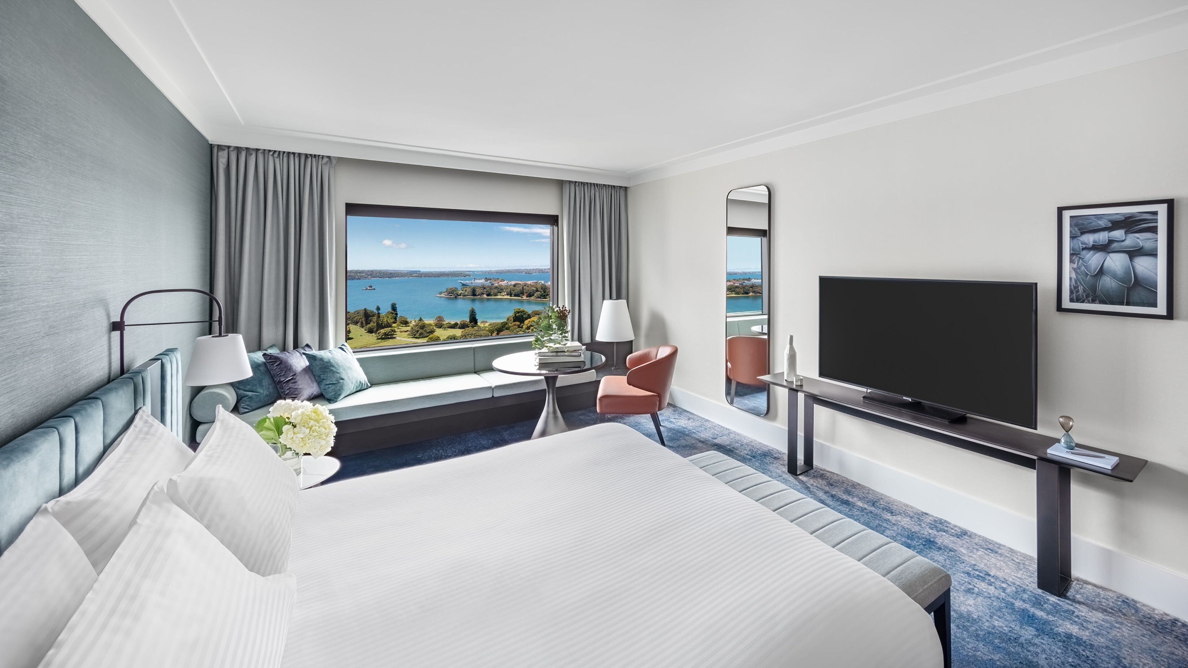 Een hotelkamer met een groot bed, een televisie, een zithoek met uitzicht op zee, en een balkon.