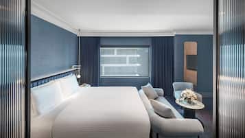 Una habitación de hotel moderna con una cama grande, un área de descanso con una mesita pequeña y un ventanal amplio.