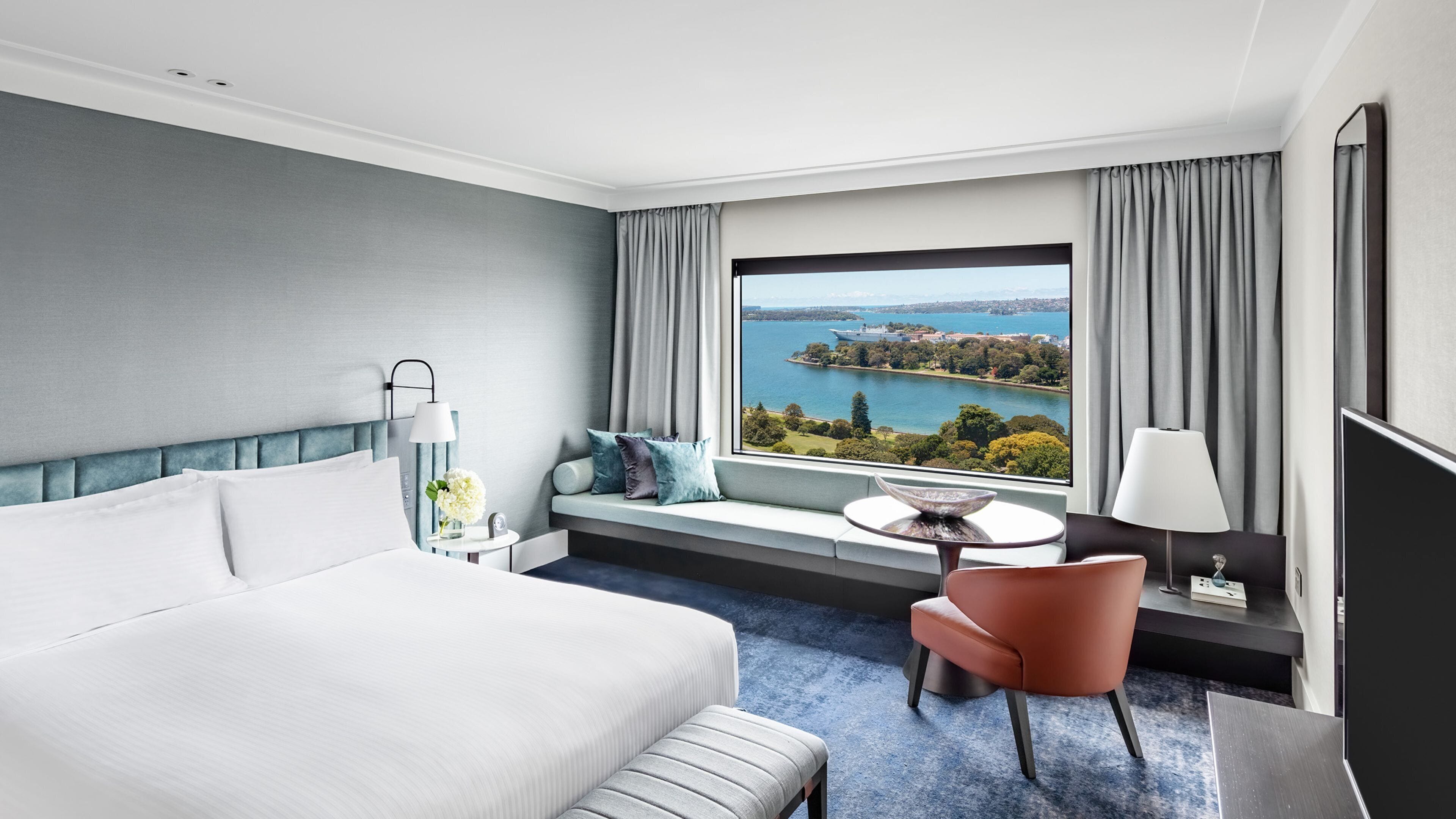 Een hotelkamer met een groot bed, een bureau met stoel, uitzicht op een meer en een raam met gordijnen.