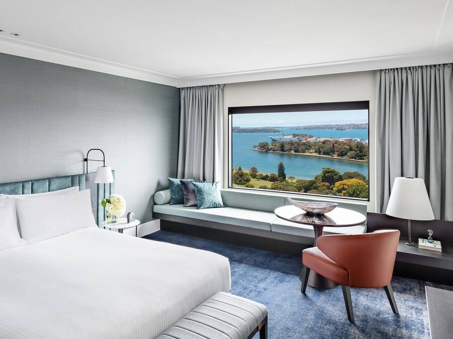 Een hotelkamer met een groot bed, een bureau met stoel, uitzicht op een meer en een raam met gordijnen.
