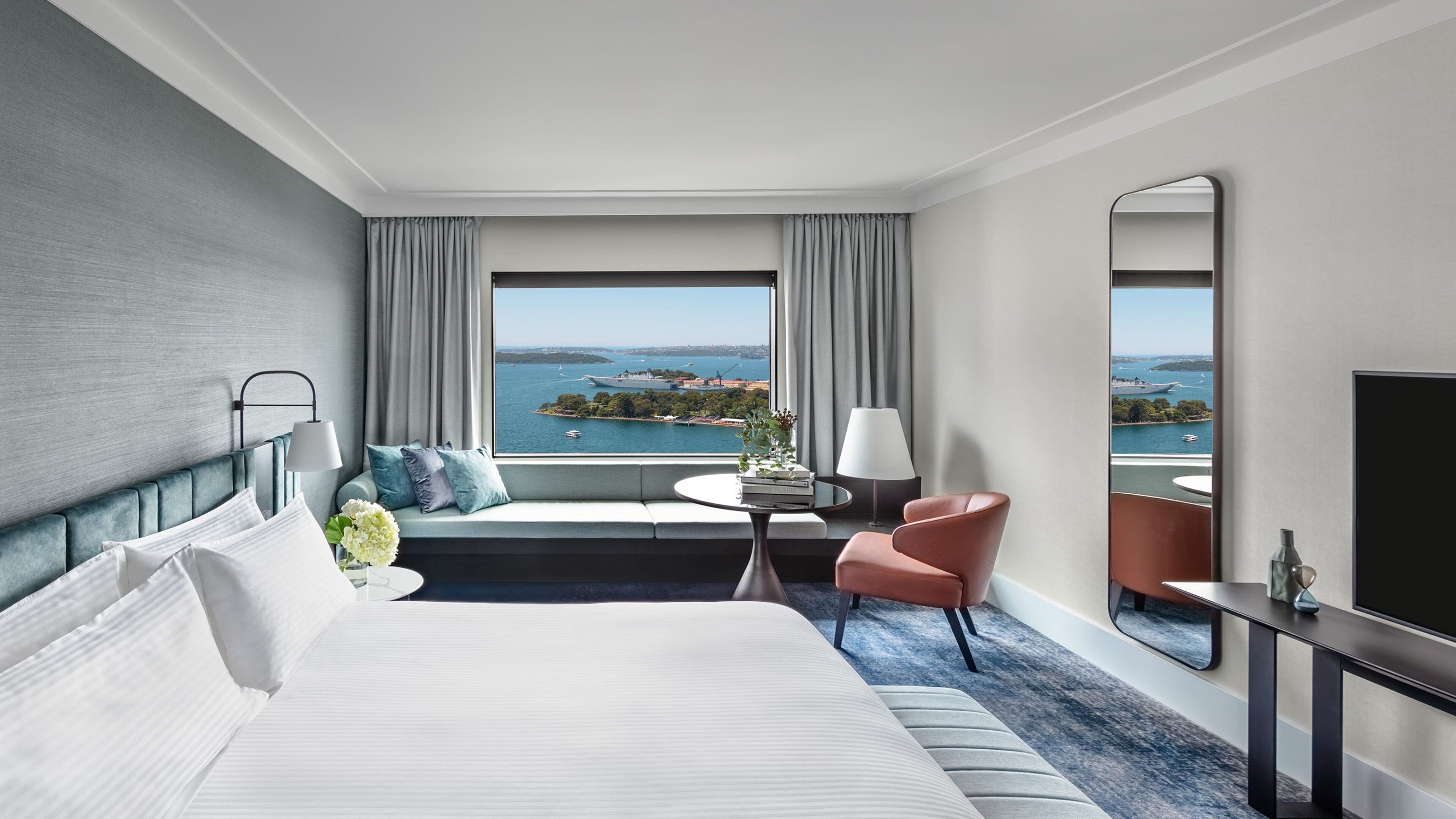 A hotel room with a large bed, a seating area with a view, a small table, and a mirror.