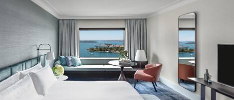 Une chambre d’hôtel avec un grand lit, un coin salon avec vue, une petite table et un miroir.