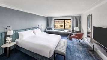 Quarto de hotel com cama grande, área de estar com vista, televisão e janela com cortinas.