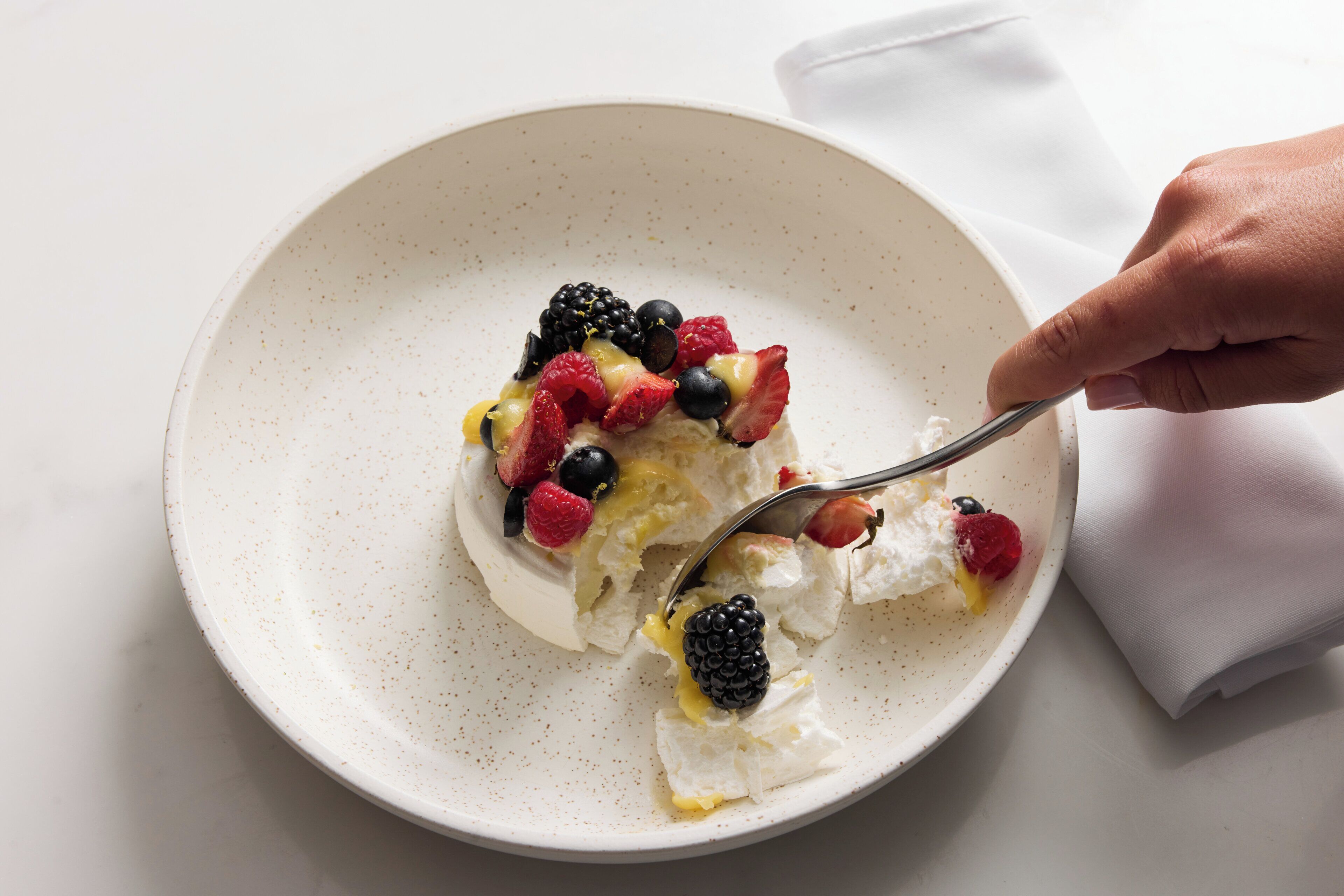 A white plate with a dessert topped with berries and a spoon.