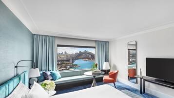 A hotel room with a large bed, a TV, a seating area with a view of a cityscape and a bridge.