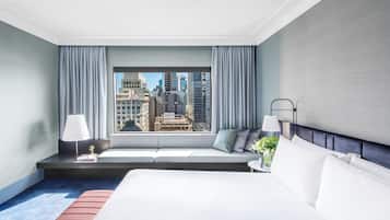 Una habitación de hotel con una cama grande, un área de descanso con vistas a la ciudad y una mesita de noche con una lámpara.