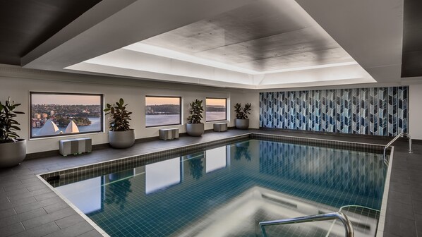 Una piscina interior moderna con grandes ventanales que ofrecen vistas a la ciudad, plantas en macetas y una pared decorativa.