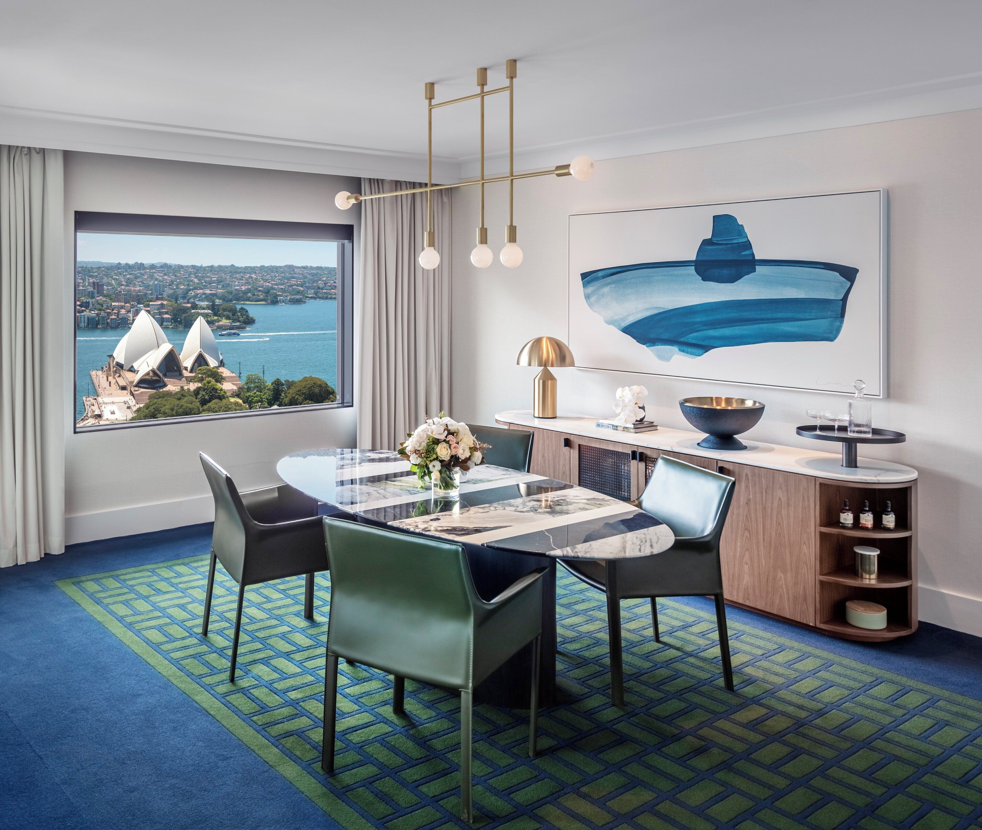 A hotel room with a dining area, a view of a cityscape, and a large painting.