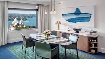 A hotel room with a dining area, a view of a cityscape, and a large painting.