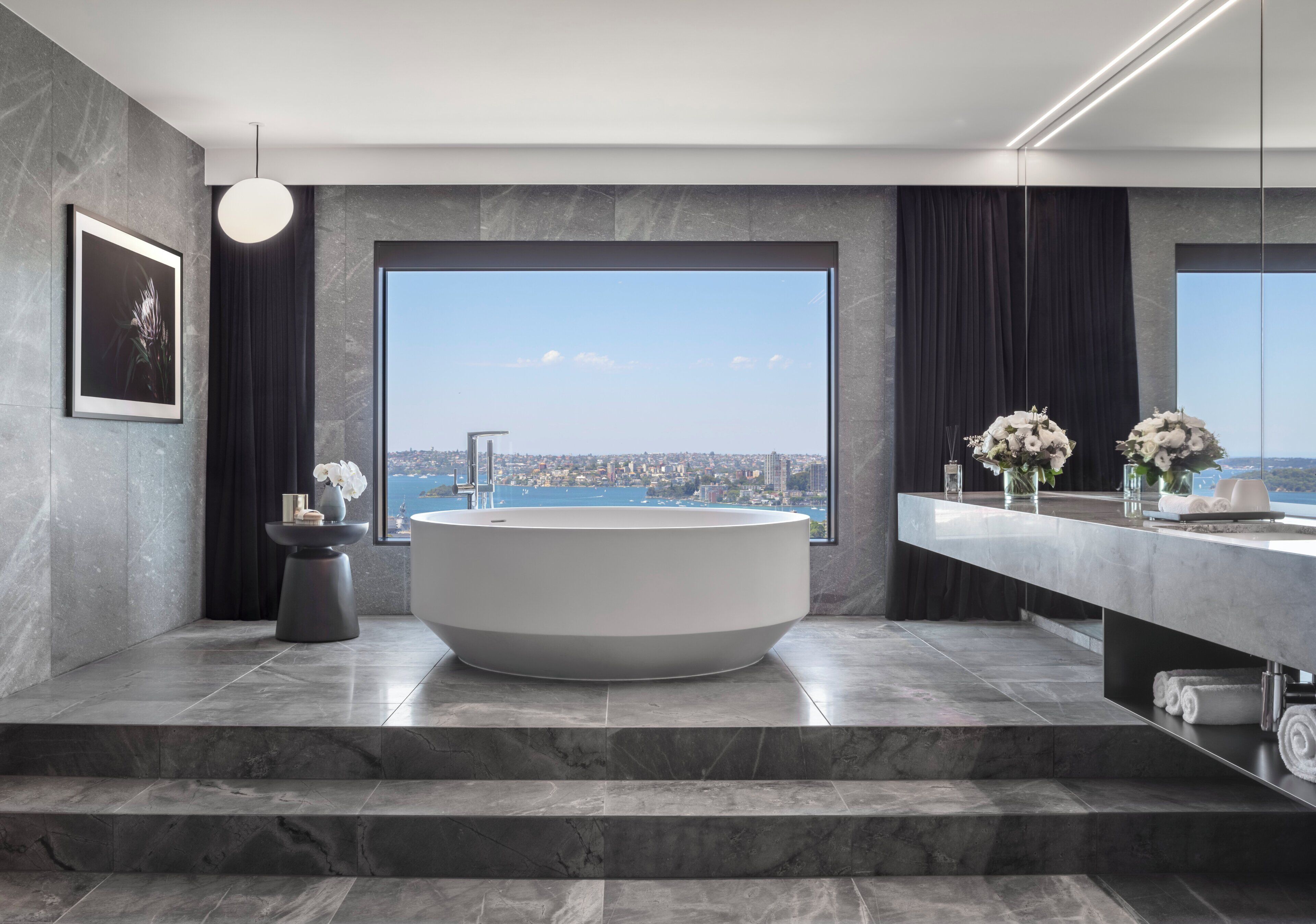 Un baño moderno con una bañera grande, vistas de la ciudad y suelo de mármol.