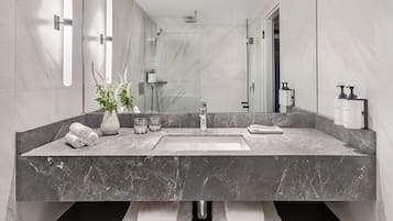 A modern bathroom with a large mirror, marble countertops, a built-in shower, and a towel rack.