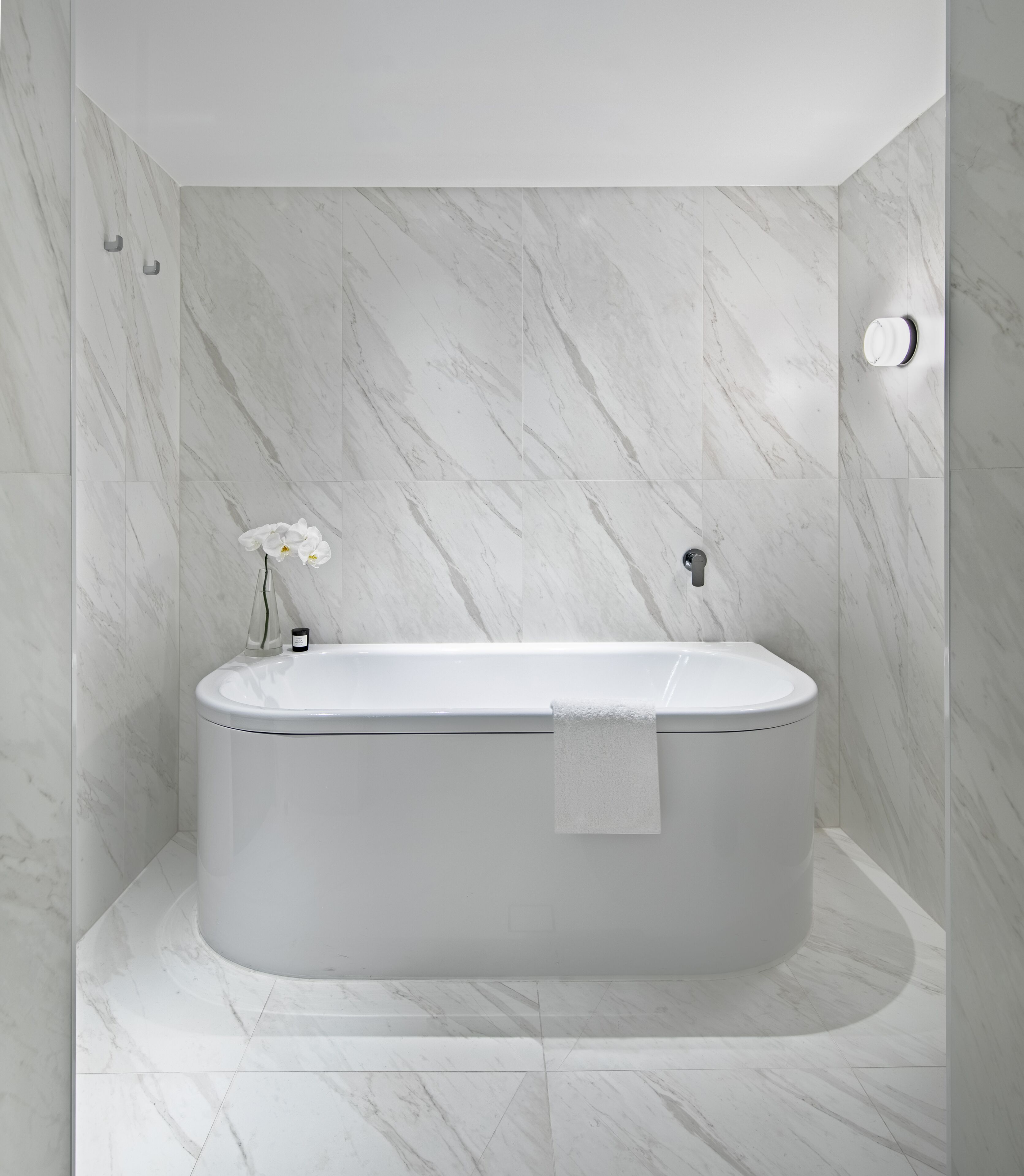 A modern bathroom with a freestanding bathtub, marble walls, and a small orchid vase.