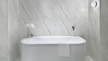 A modern bathroom with a freestanding bathtub, marble walls, and a small orchid vase.