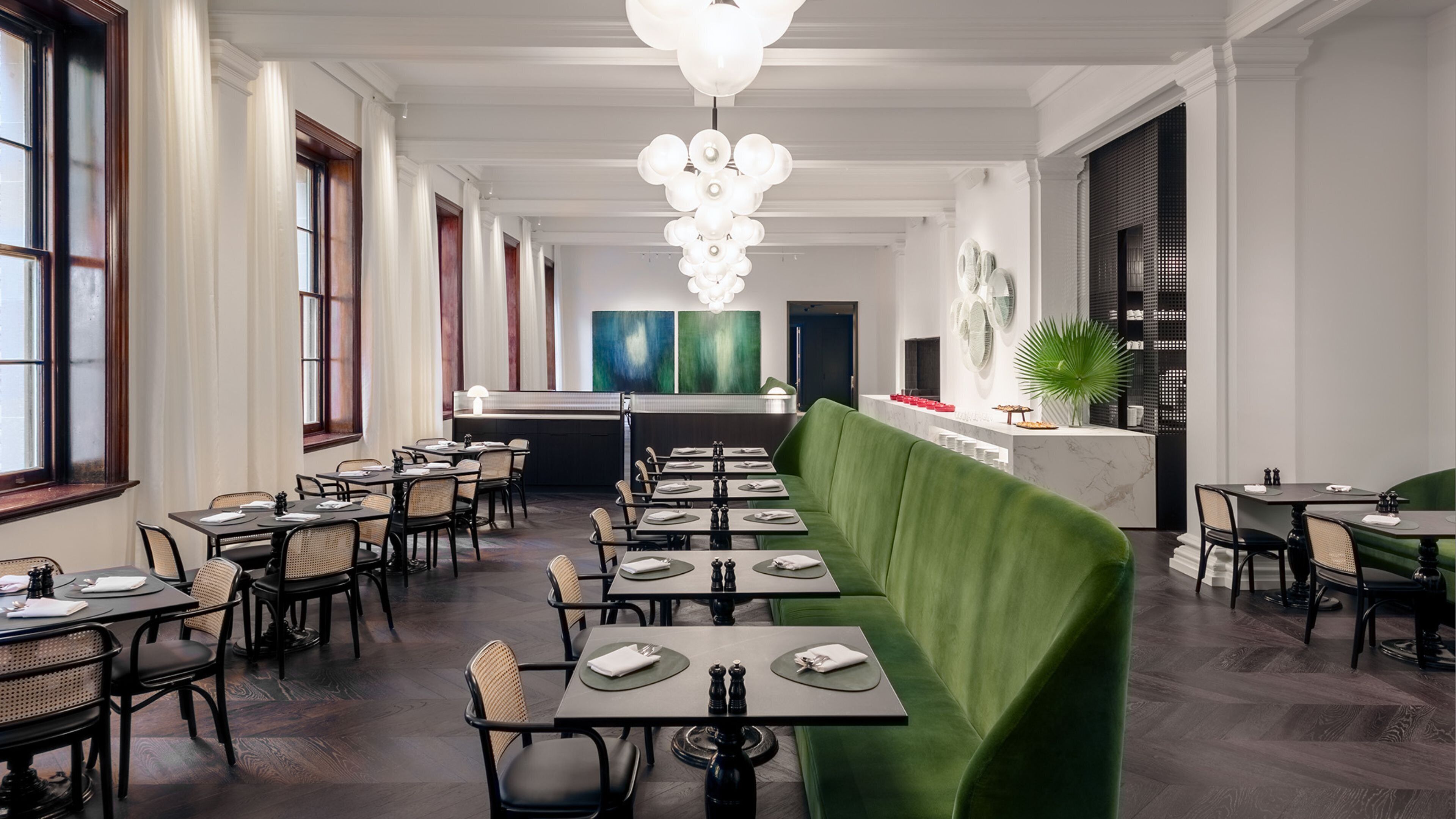 A restaurant with a long counter, multiple tables, and a green upholstered bench.