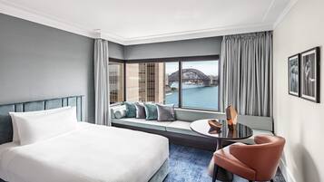 Habitación de hotel con una cama, una zona de estar con cojines, una mesa redonda y vistas a un puente.