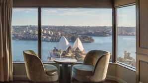 A room with a large window overlooking a cityscape, two chairs, and a small table with glasses. - InterContinental Sydney by IHG (Sydney)