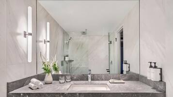 A modern bathroom with a large mirror, marble tiles, a sink, and a shower.