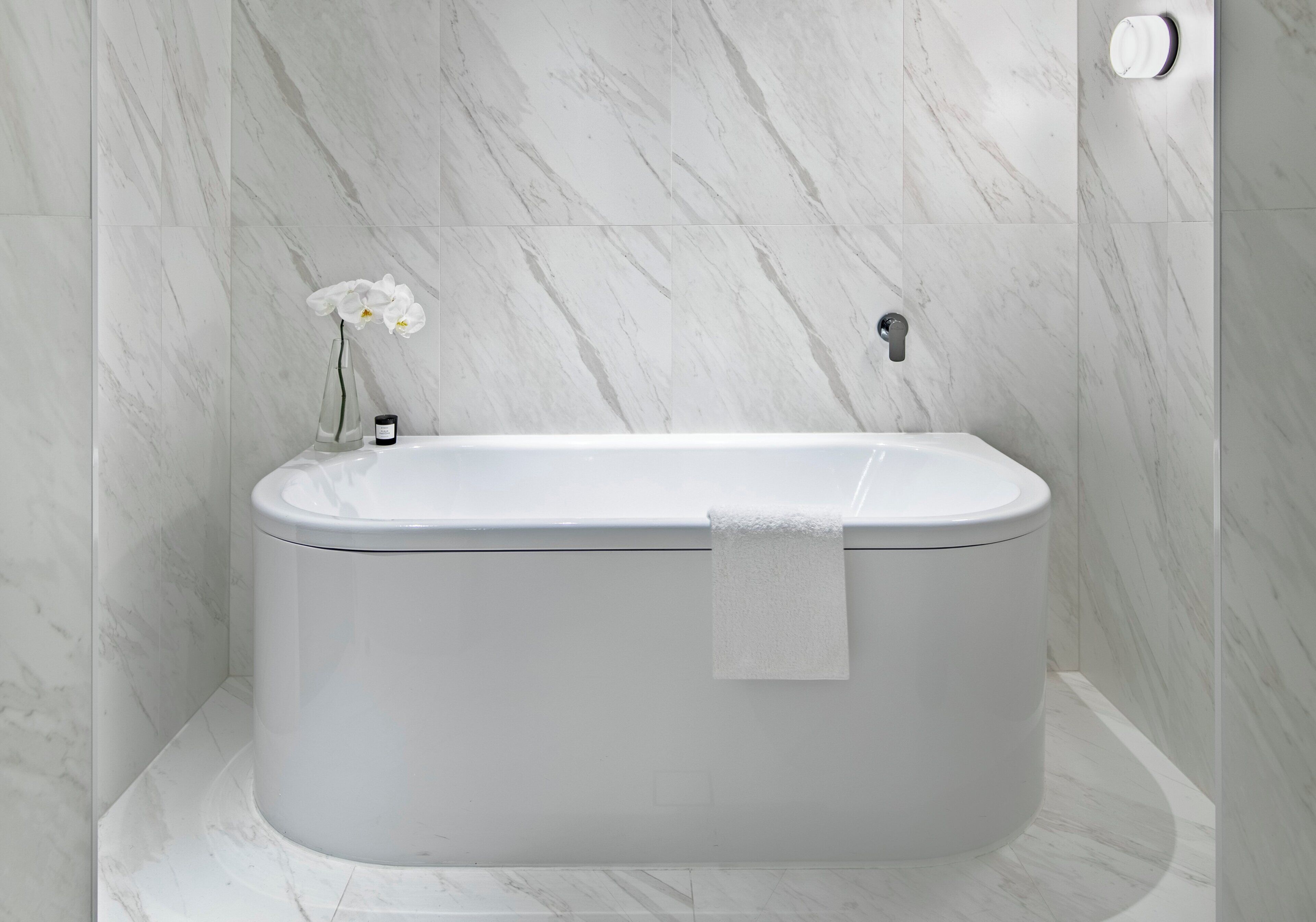 A modern bathroom with a freestanding bathtub, marble walls, and a single orchid.