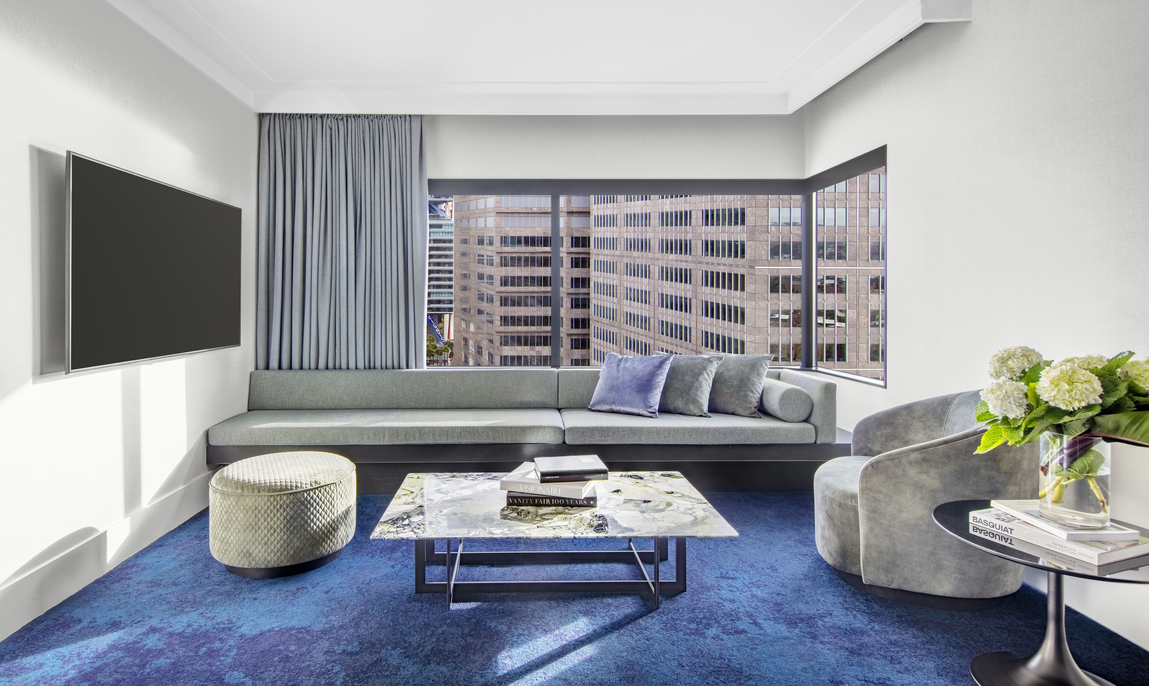 A modern living room with a sectional sofa, a coffee table, and a view of a cityscape through large windows.