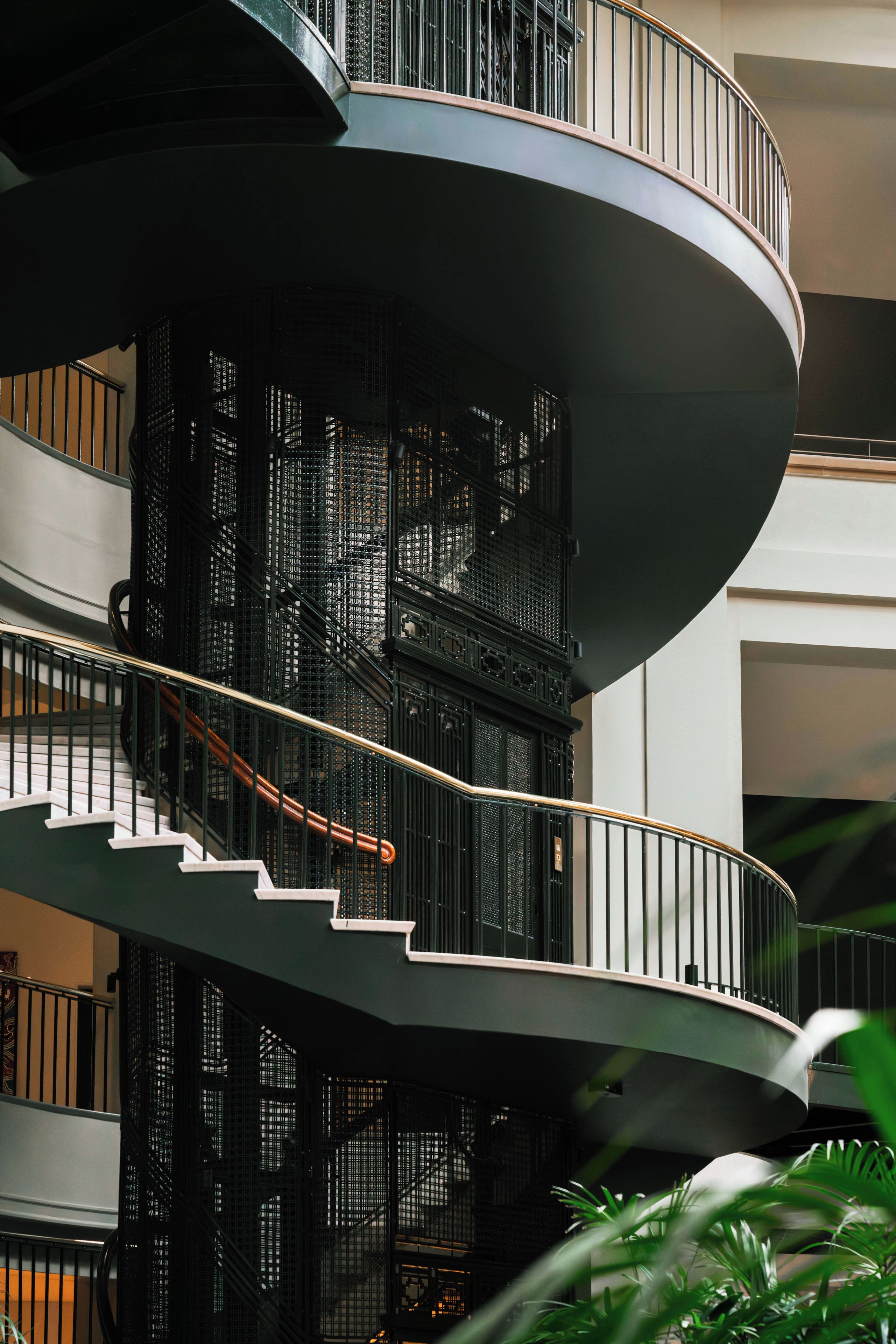 Una escalera en espiral de varios niveles con barandillas de metal y un núcleo central, rodeada por la fachada de un edificio moderno.
