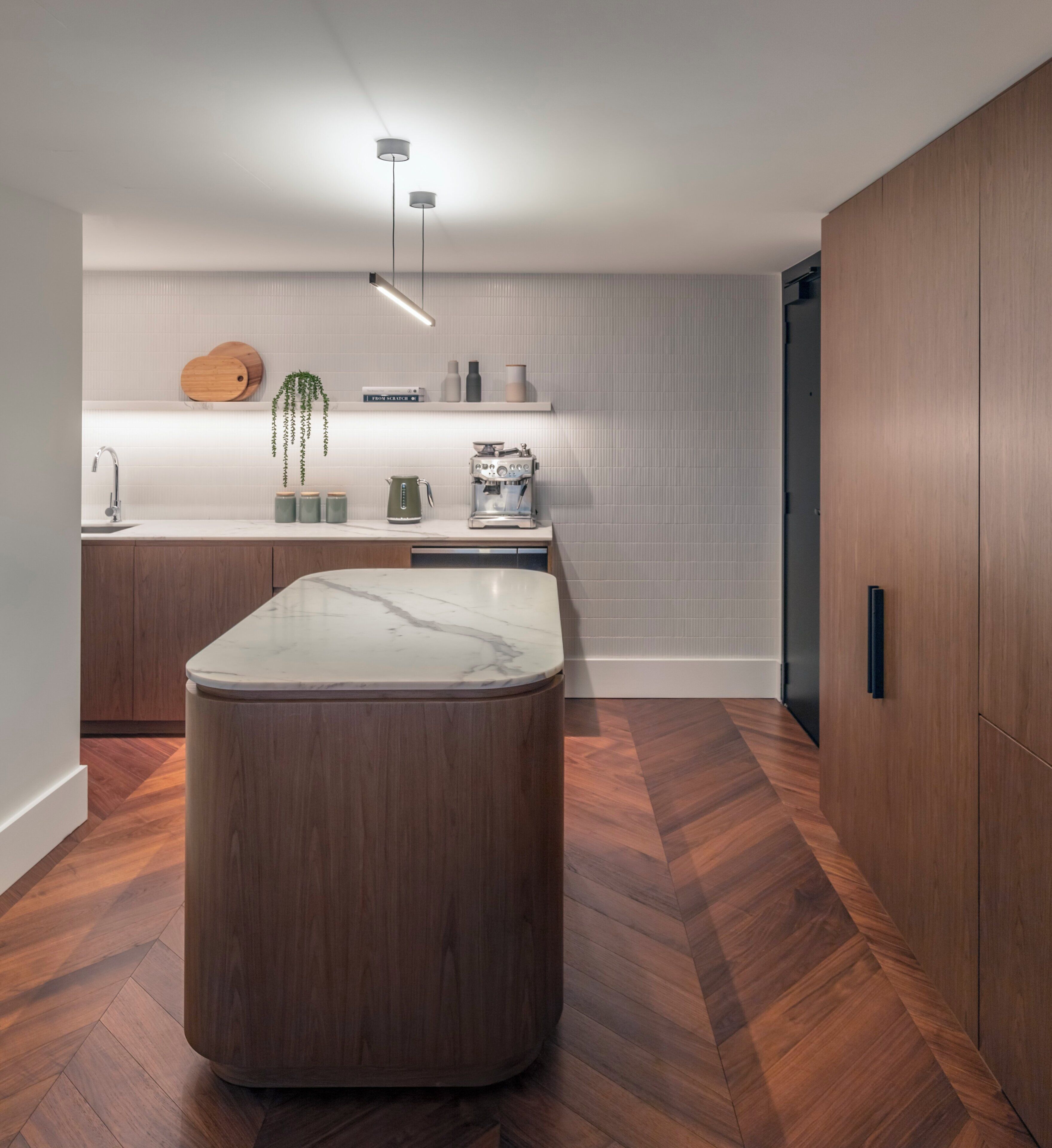 A modern kitchen with a marble countertop, wooden cabinets, and a herringbone floor pattern.