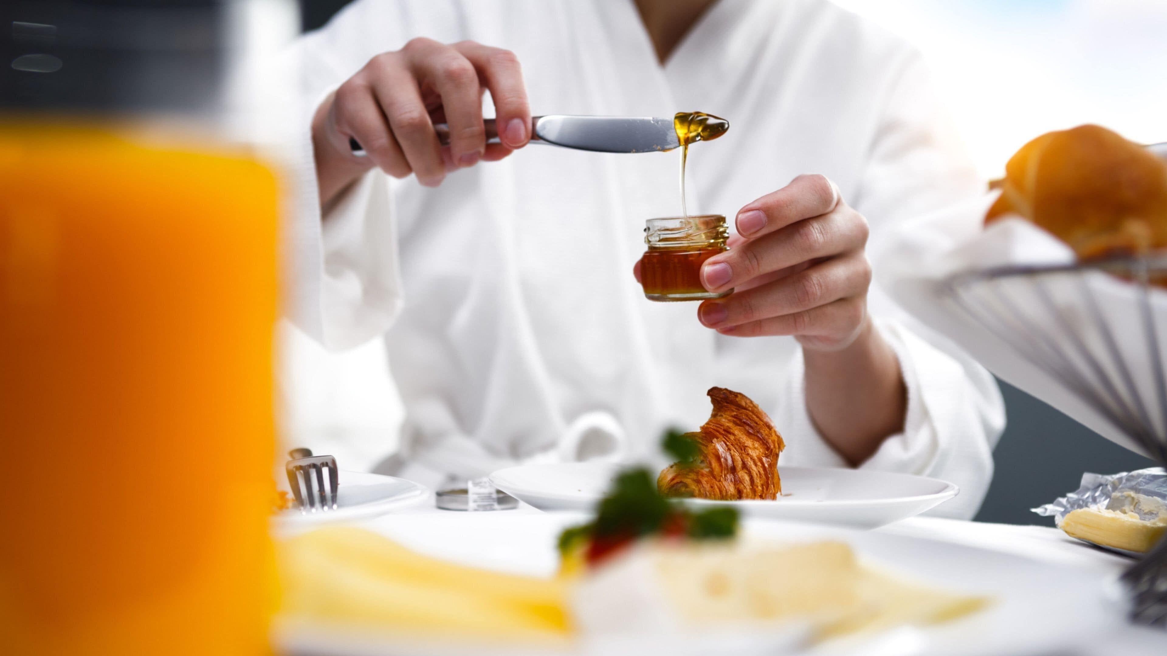 Una persona sirviendo miel de un tarro a un plato.