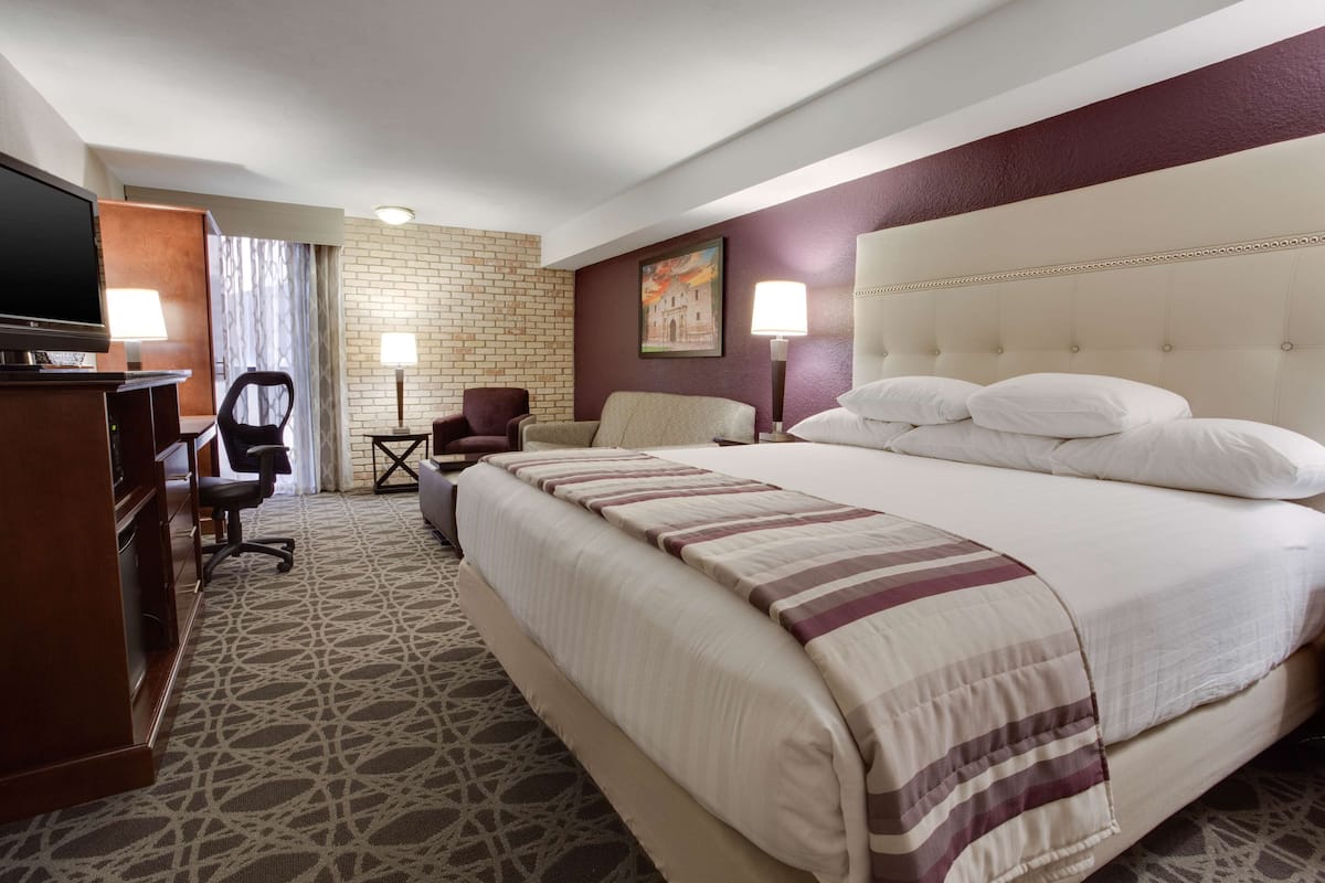 A hotel room with a large bed, a desk with a television, a chair, and a lamp.