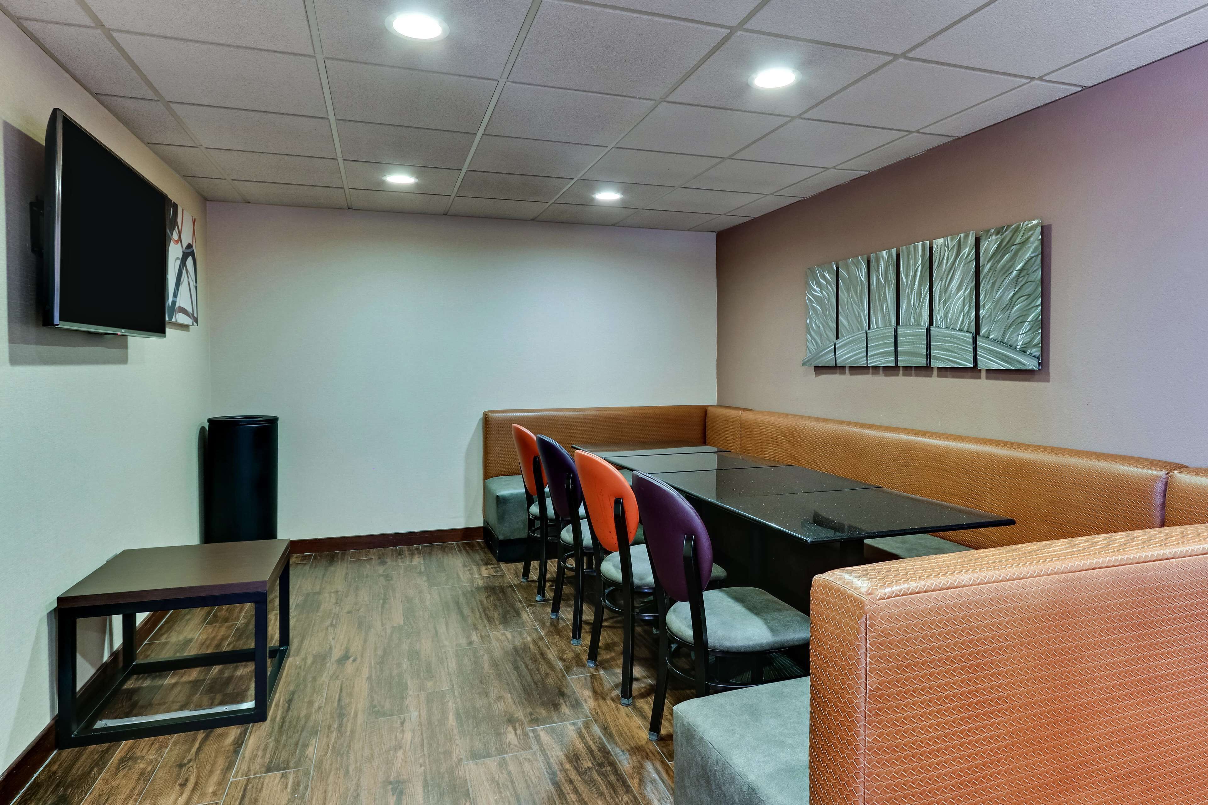 Un salón de conferencias con una mesa de vidrio, varias sillas, un sofá, un televisor y un cubo de basura.