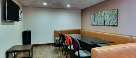 Un salón de conferencias con una mesa de vidrio, varias sillas, un sofá, un televisor y un cubo de basura.