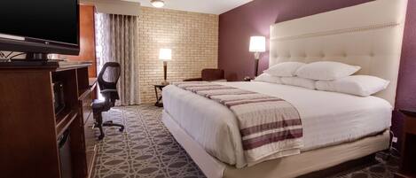 Quarto de hotel com uma cama grande, televisão, escrivaninha e uma cadeira.