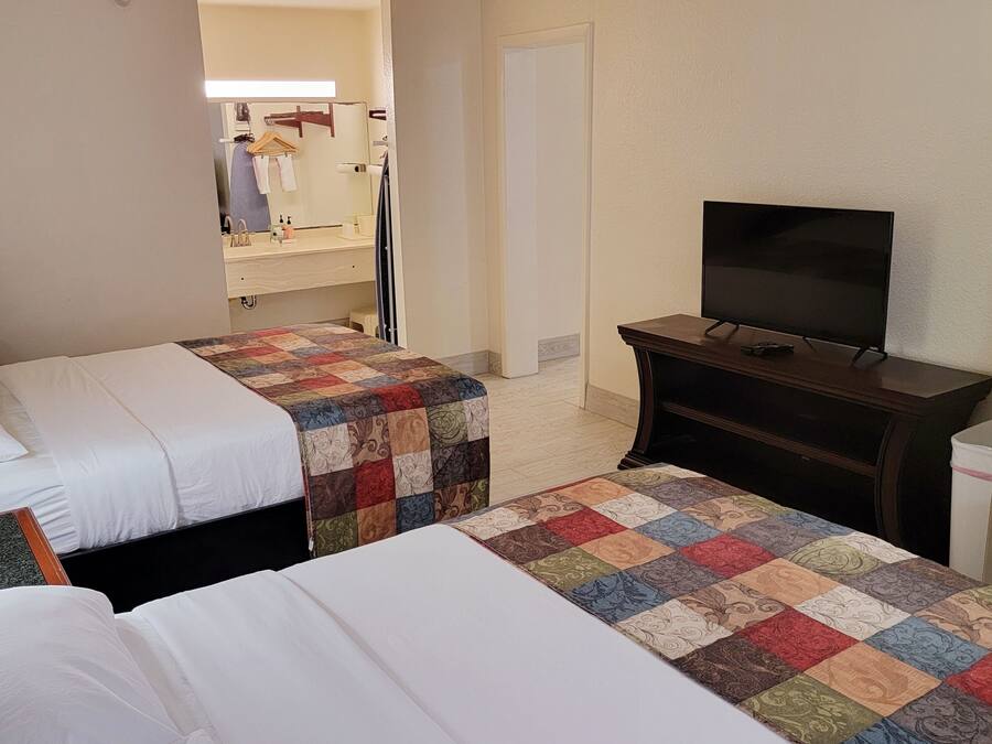 Ein Hotelzimmer mit zwei Betten, einem Fernseher, einem Kühlschrank und einem sichtbaren Badezimmer hinter einer offenen Tür.