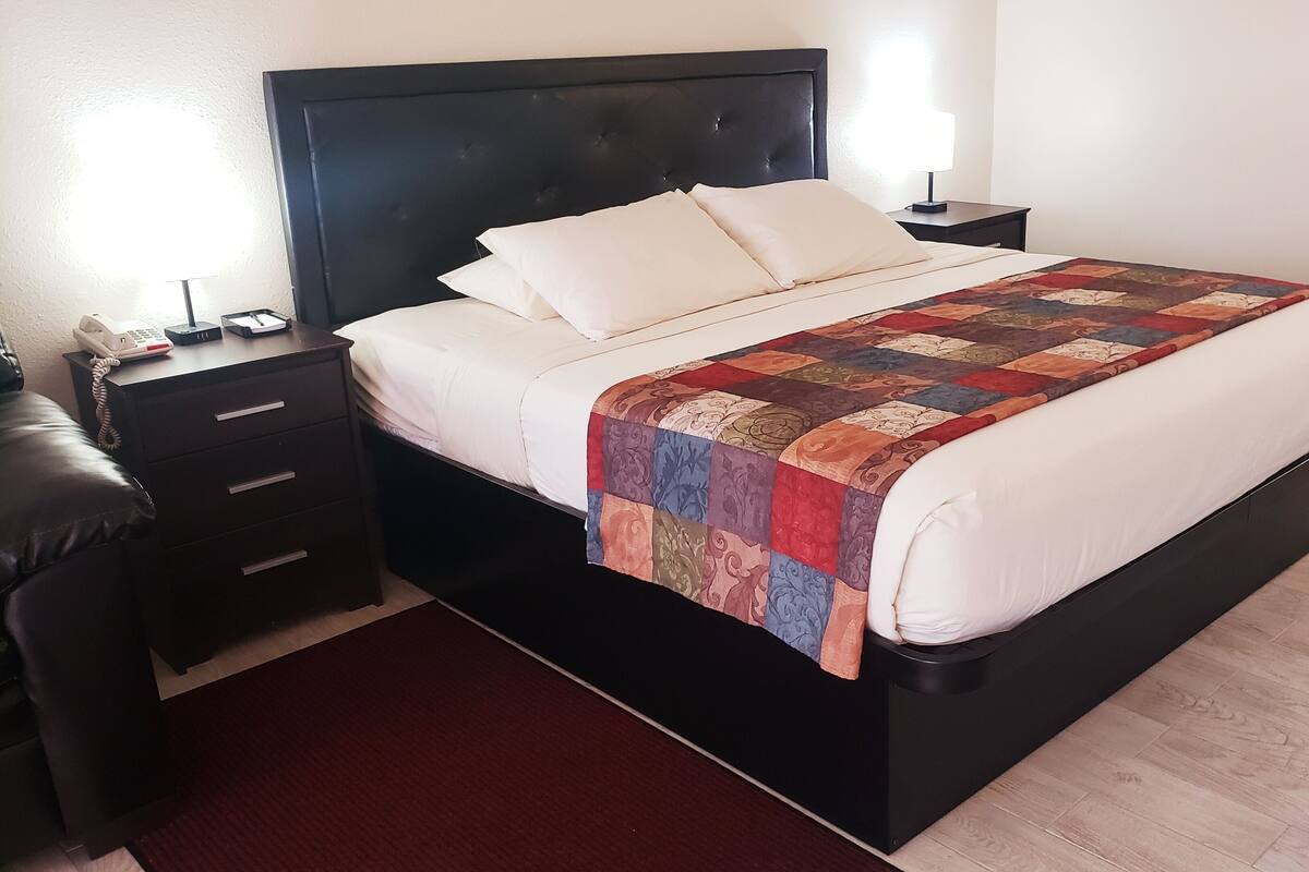 A neatly made bed with a quilt, a bedside table with a lamp, and a telephone on the nightstand.