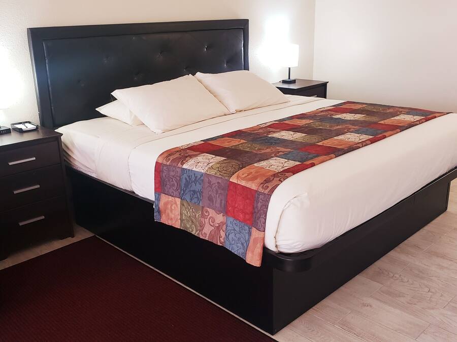 A neatly made bed with a quilt, a bedside table with a lamp, and a telephone on the nightstand.