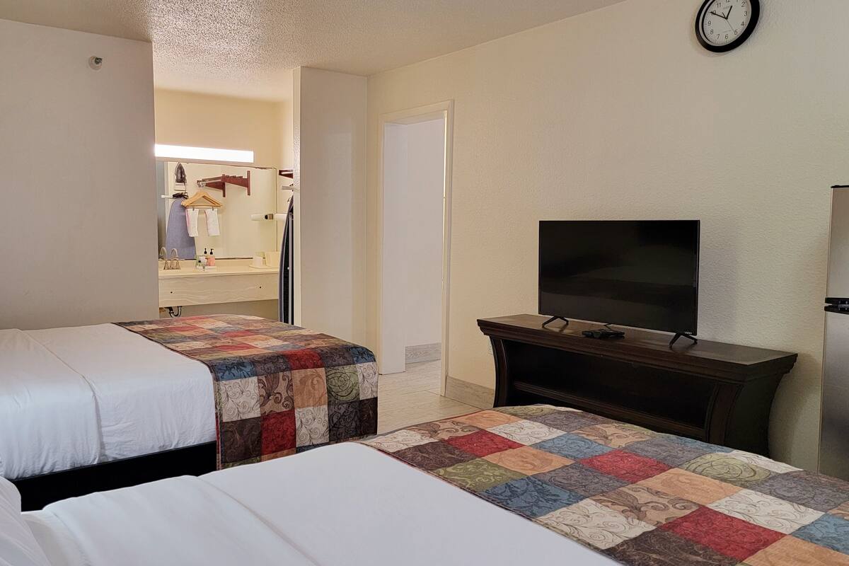 A hotel room with two beds, a television on a wooden stand, and a refrigerator.