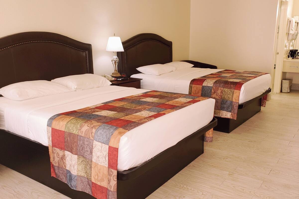 Two twin beds with a quilt, a bedside table with a lamp, and a small desk with a telephone.