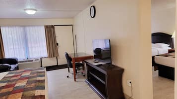 Una habitación de hotel con cama, escritorio con computadora, silla, ventana con cortinas y un reloj en la pared.