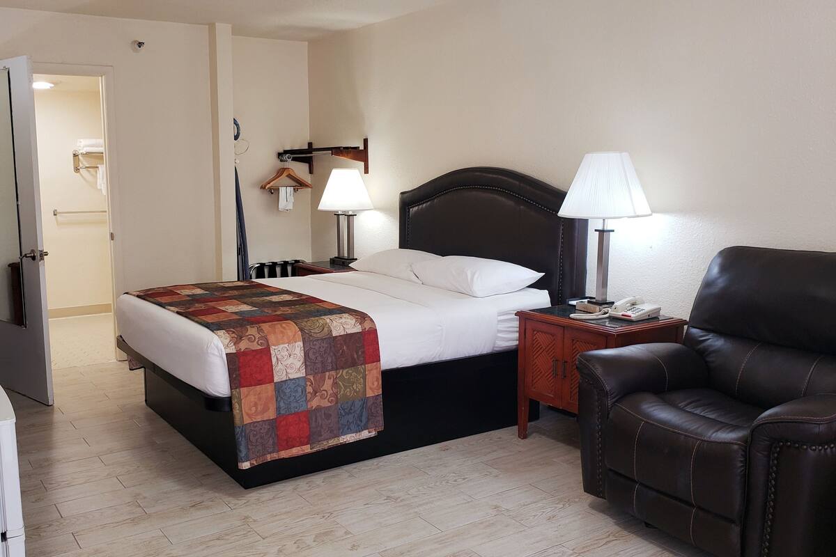 A hotel room with a bed, a chair, a desk, and a lamp.