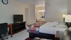 A hotel room with a bed, a desk with a television, a chair, and a clock on the wall. - Simple Rewards Inn (Hilton Head Island)