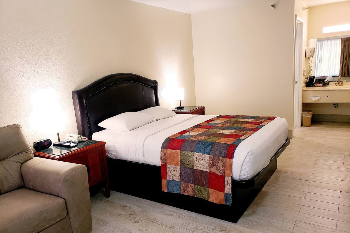 A hotel room with a bed, bedside table, lamp, and a chair.
