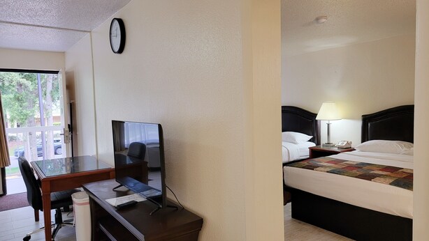 A hotel room with a desk, chair, TV, bed, and a clock on the wall. - Simple Rewards Inn (Hilton Head Island)