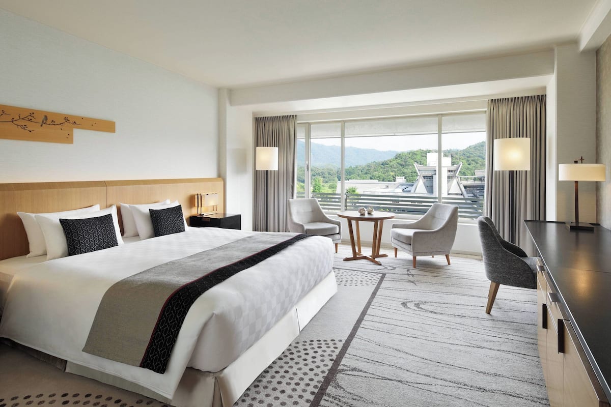 Ein Hotelzimmer mit einem großen Bett, zwei Sesseln, einem kleinen Tisch und Blick auf die Berge.