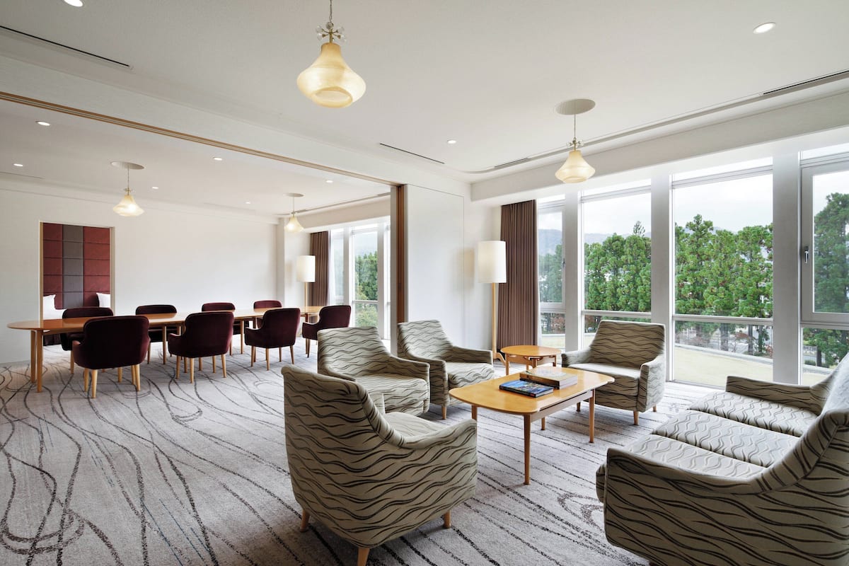 Ein geräumiges Hotelzimmer mit großem Fenster, einem Essbereich mit Tisch und Stühlen sowie mehreren gemusterten Sesseln.
