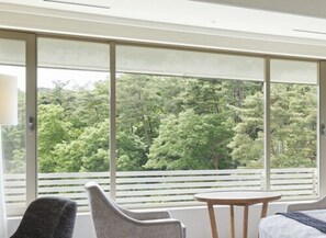 Enjoy a peaceful forest view from the comfort of this room, featuring a bed with a white headboard and a small table for two.