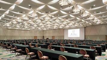 A conference room with rows of tables and chairs, a large screen, and a ceiling with unique lighting fixtures.