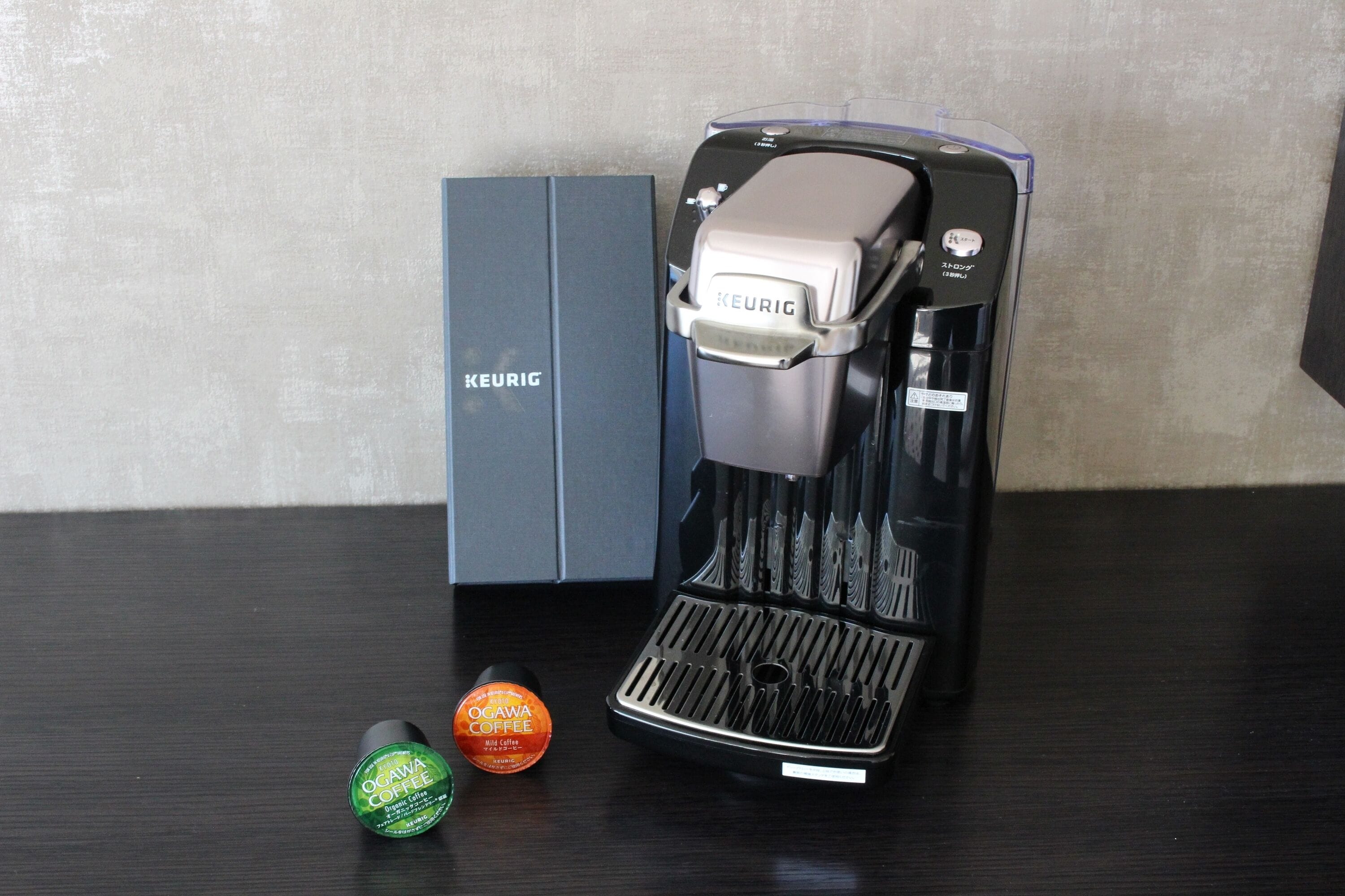 A Keurig coffee maker with a box and two coffee pods on a dark surface.
