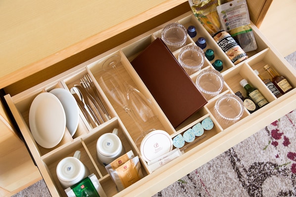 Un cajón con utensilios de cocina ordenados, incluyendo platos, tazones, tazas y una copa de vino.