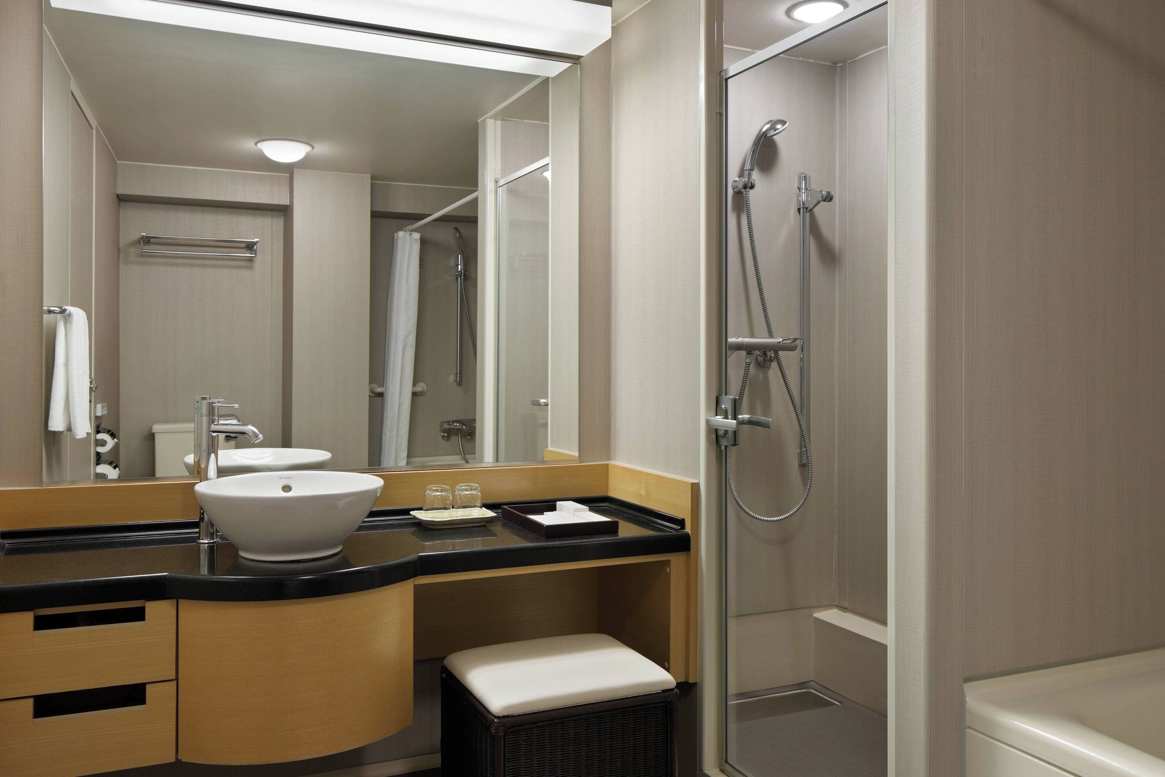 A modern bathroom with a large mirror, a sink, a shower, and a bench.