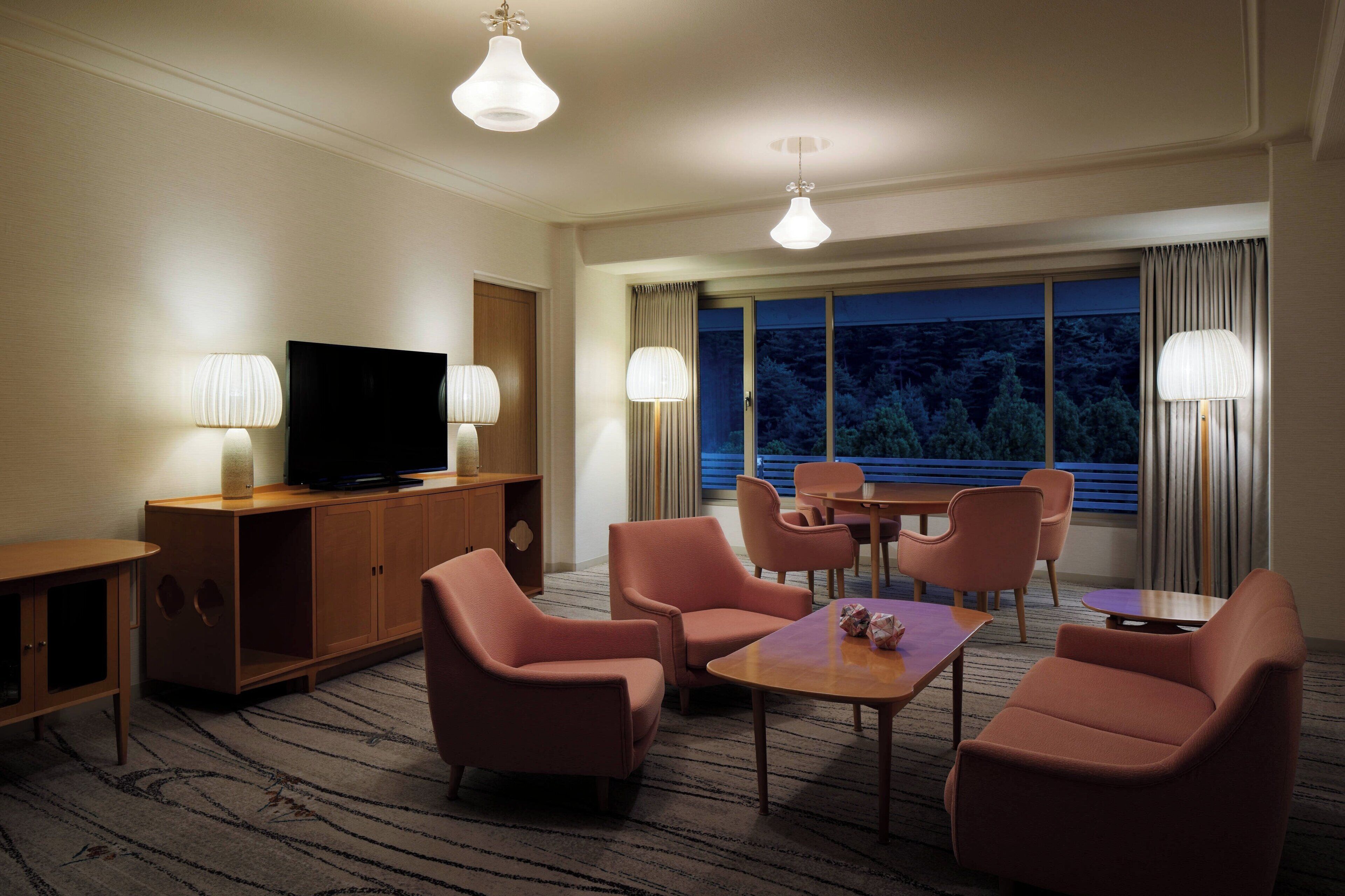 A hotel room with a television, a wooden cabinet, a sofa, a coffee table, and a dining area with chairs and a table.