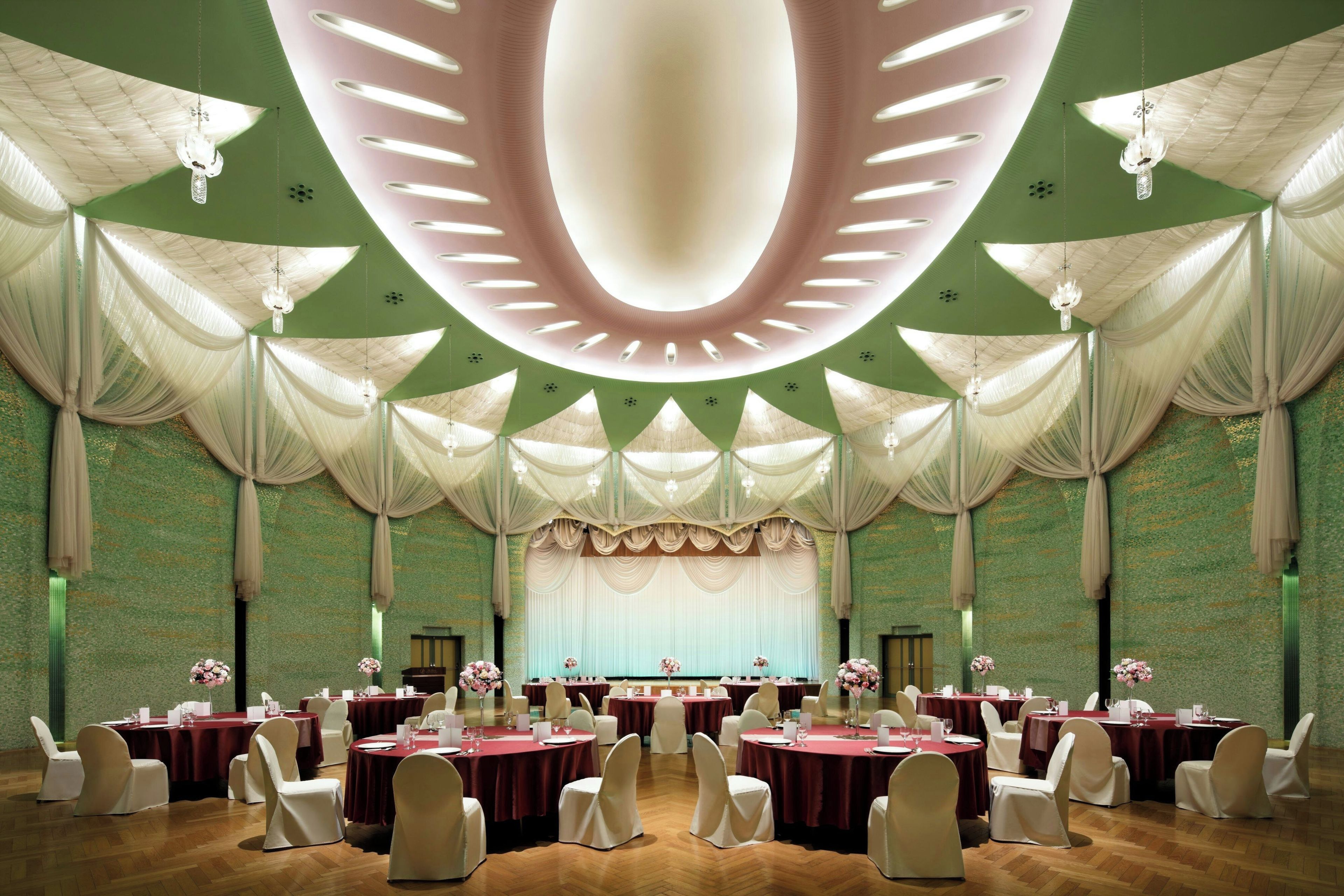 A banquet hall with round tables, white chairs, and a stage with draped curtains.